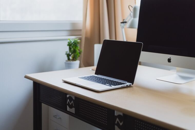 Bright desk with a laptop and an iMac beside a window